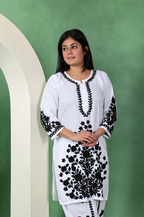 Woman wearing a white kurta with black floral embroidery against a green background