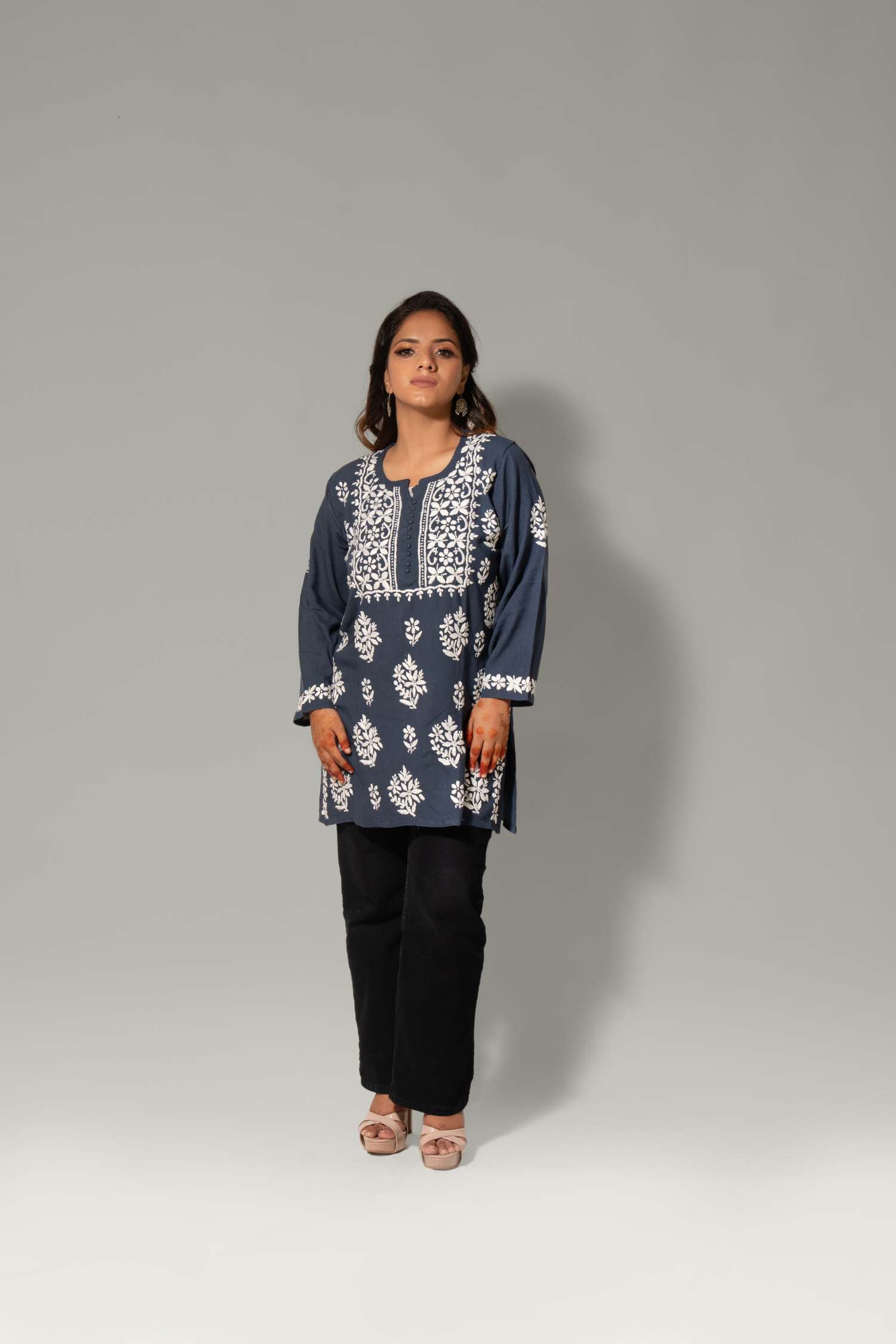 A woman modeling a navy blue kurta with intricate white embroidery, paired with black pants, standing against a neutral gray studio background.