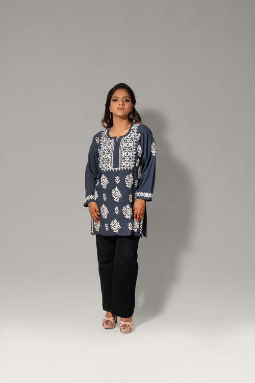 A woman modeling a navy blue kurta with intricate white embroidery, paired with black pants, standing against a neutral gray studio background.